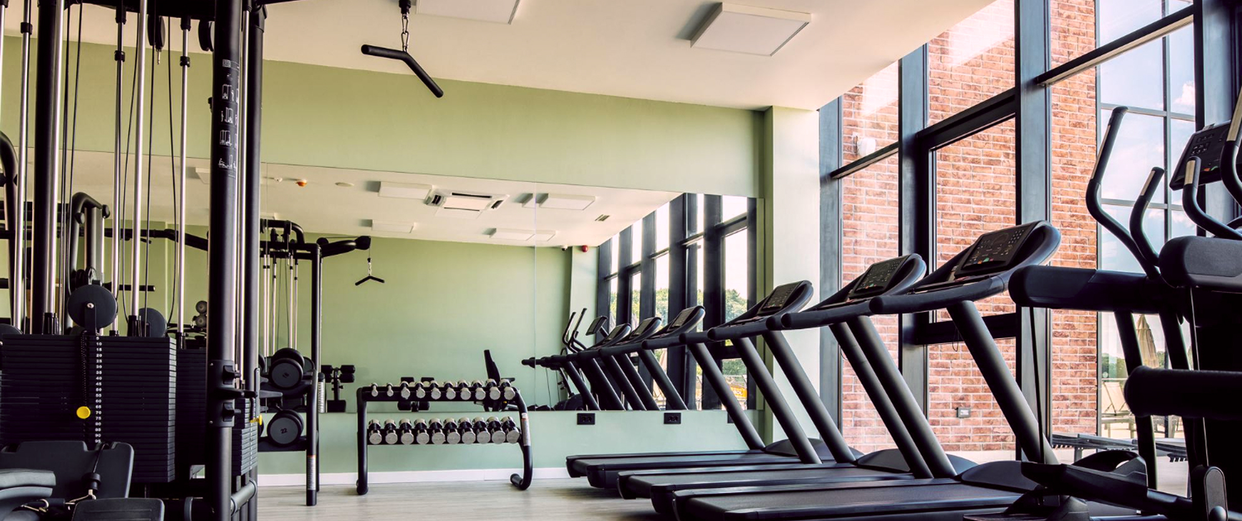 фото спортзала, справа беговые дорожки, слева тренажеры, посередине гантели